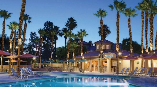 Relax by the pool surrounded by palm trees and enjoy the adjacent seating area with tables and chairs.