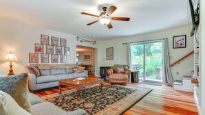 A spacious living room with a ceiling fan, a fireplace, a large window with curtains, and a staircase. - Londonderry Retreat ~ 3 Mi to Lowell Lake! (Londonderry)