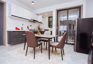 A modern kitchen with white cabinets, a dining area with a table and chairs, and a refrigerator. - Tastefully furnished 3 bedroom apartment in  Kilimani (Nairobi)
