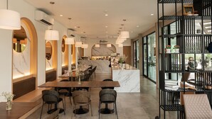 Een modern restaurantinterieur met een marmeren bar, houten tafels en zwarte metalen planken.