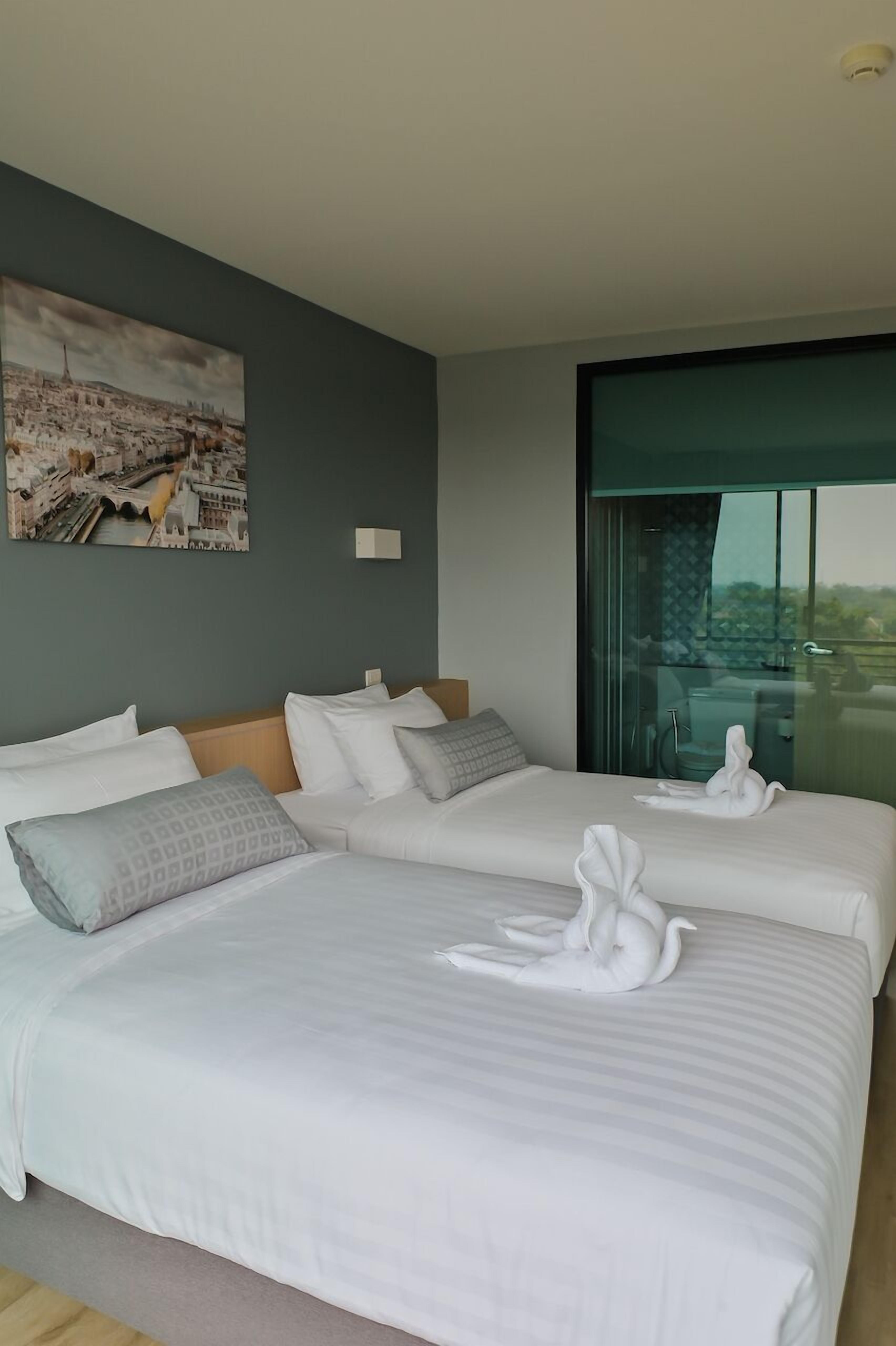 A hotel room with two beds, a cityscape painting, and a large window with a view.