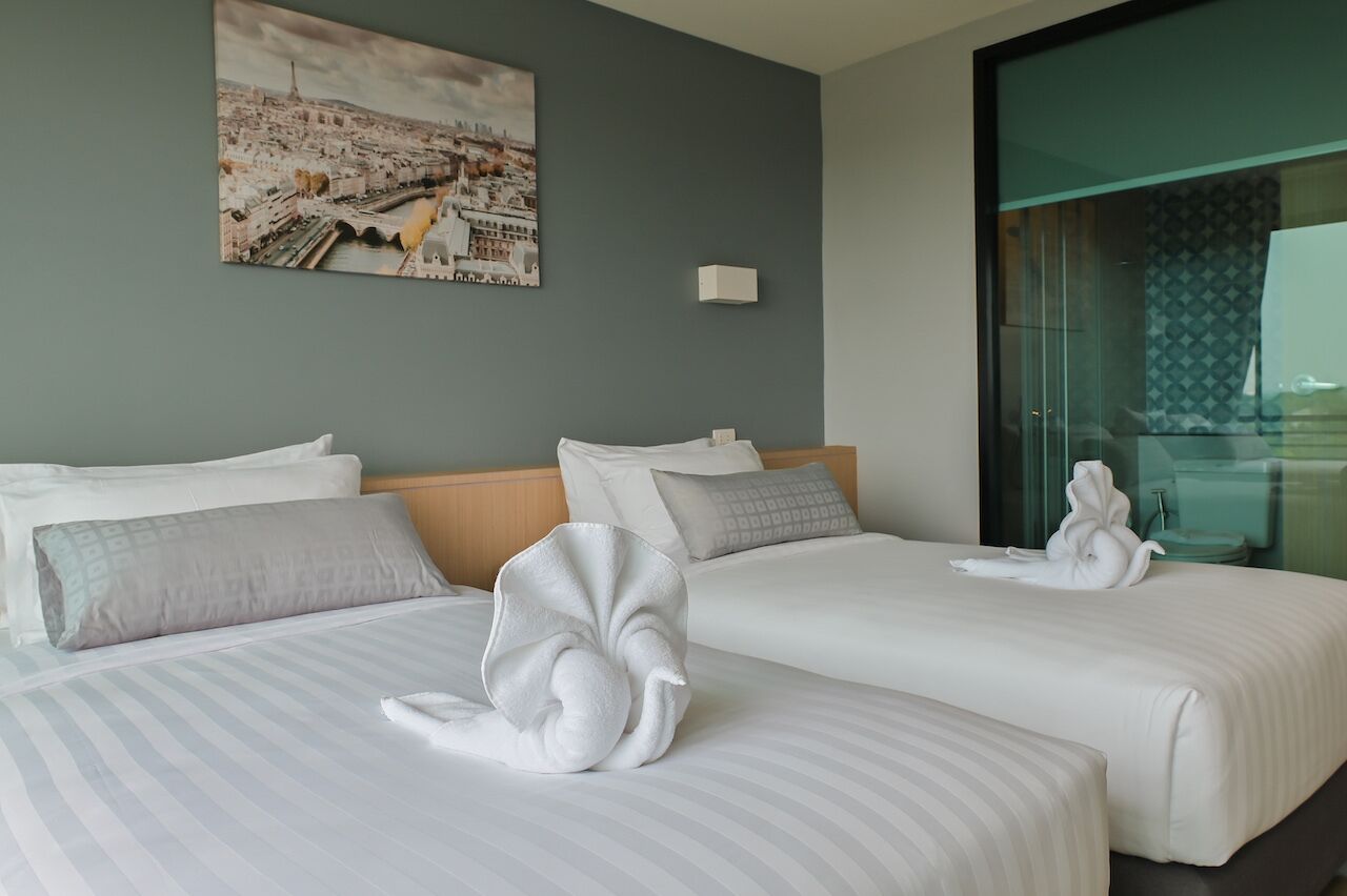 A hotel room with two beds, a large window, and a cityscape painting on the wall.