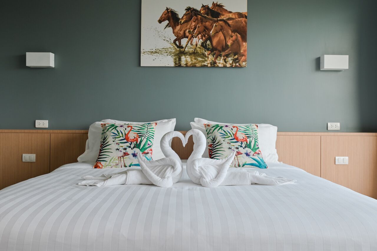 Habitación de hotel con una cama, dos almohadas con diseño tropical, una toalla dispuesta en forma de corazón y un cuadro de caballos en la pared.