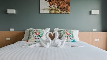 A hotel room with a bed, two pillows with a tropical design, a heart-shaped towel arrangement, and a painting of horses on the wall.