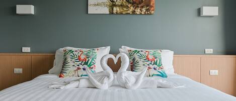 Habitación de hotel con una cama, dos almohadas con diseño tropical, una toalla dispuesta en forma de corazón y un cuadro de caballos en la pared.