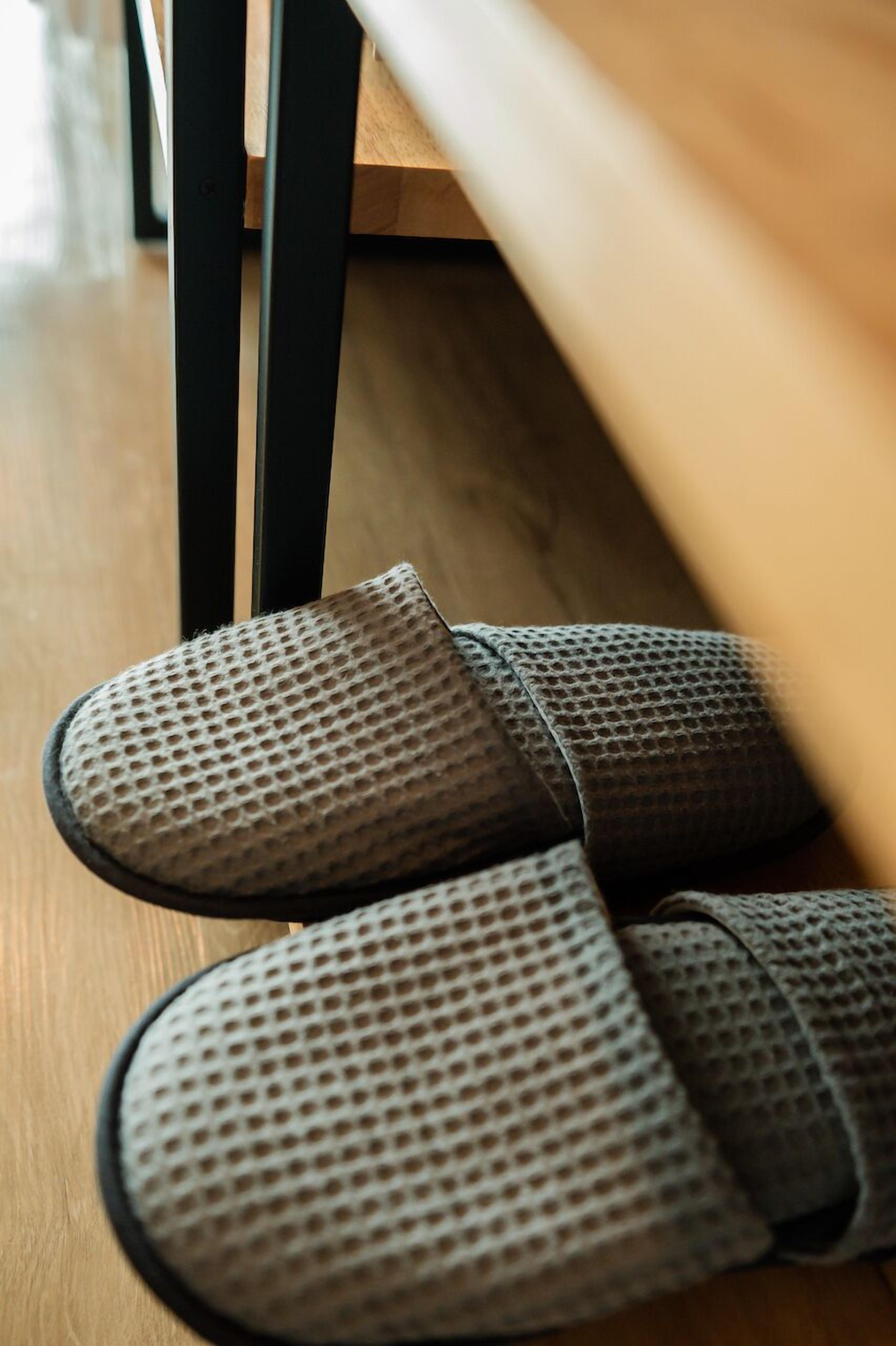 A pair of grey, perforated slippers on a wooden floor.