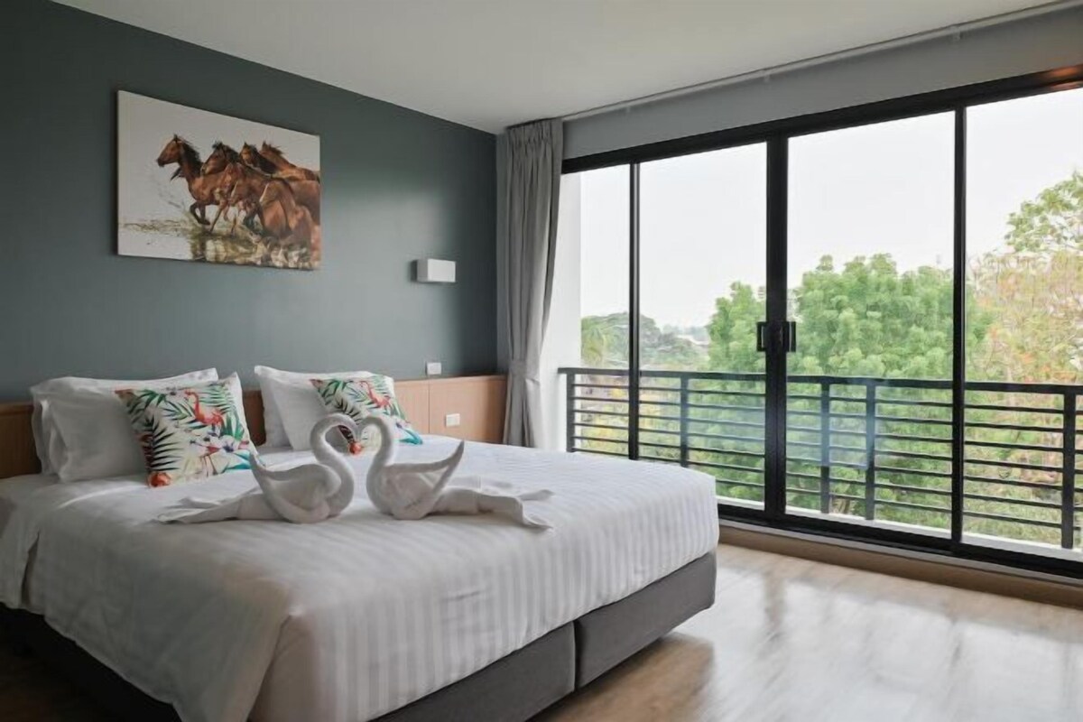 A bedroom with a large bed, a painting of horses, and a balcony with a view of trees.