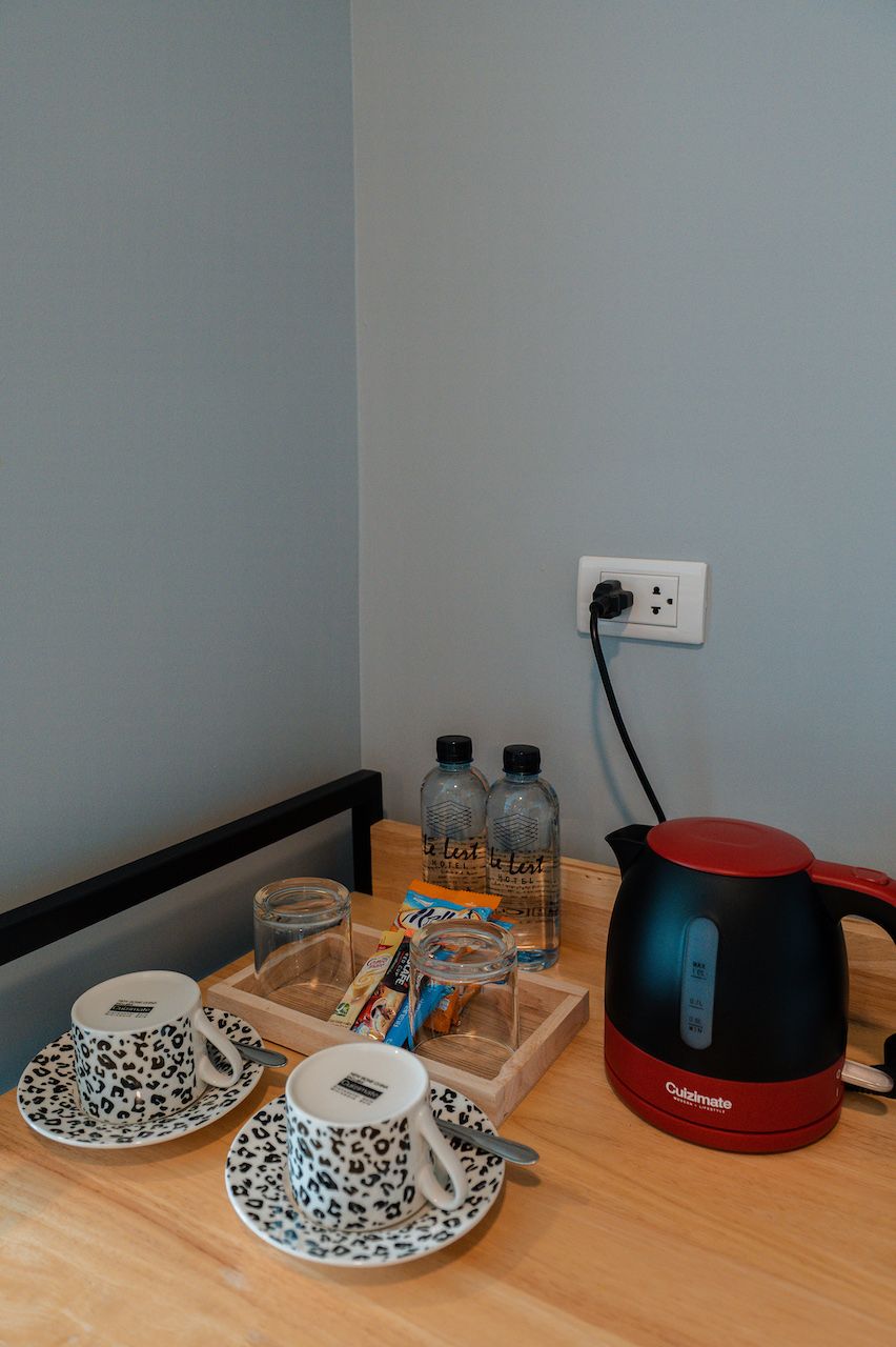 A kitchenette with a kettle, cups, and bottles on a wooden table.