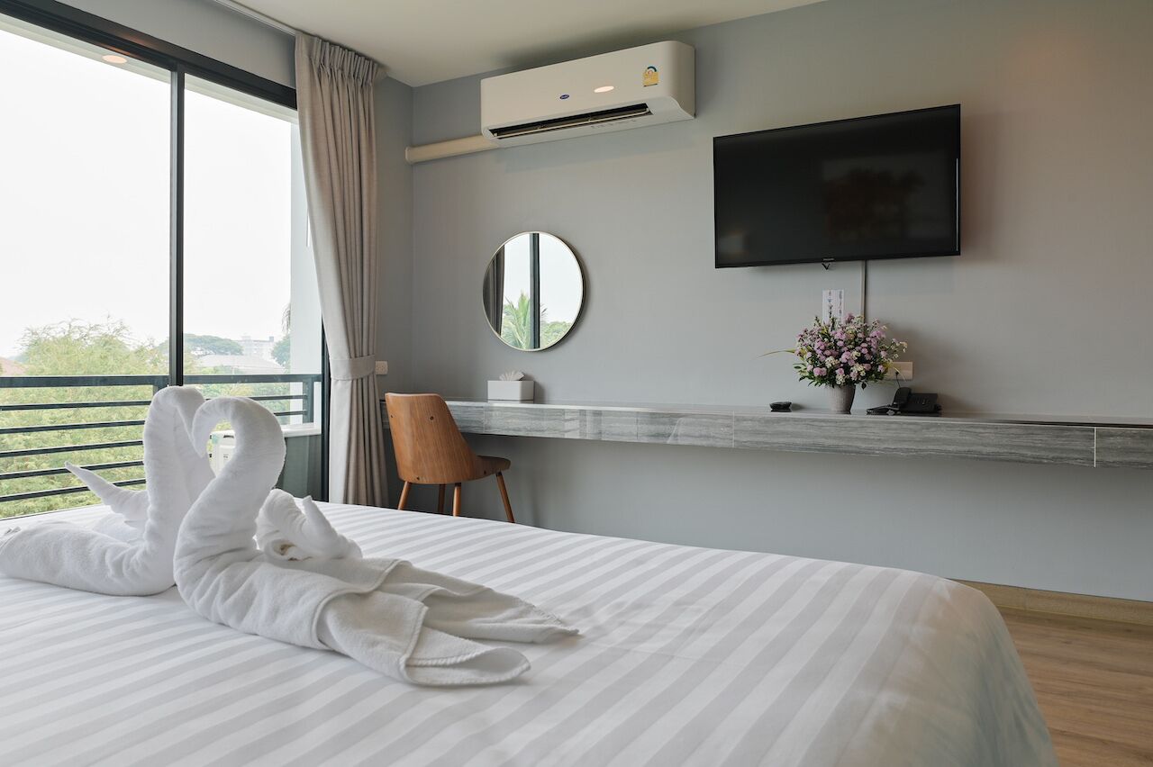 A hotel room with a bed, a TV, a mirror, and a window with curtains.