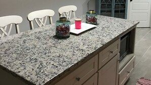 Eine Küche mit Granit Arbeitsplatten, weißen Stühlen, einem türkisblauen Schrank und einer Pendelleuchte.