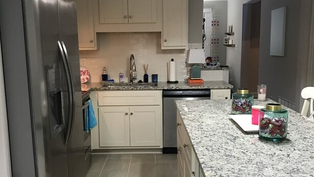 Eine moderne Küche mit weißen Schränken, einem Edelstahl-Kühlschrank, Granit-Arbeitsplatten und einem Teppich mit rosa Streifen.