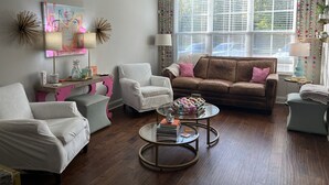 Ein Wohnzimmer mit einem braunen Ledersofa, weißen Sesseln, einem Glastisch und einem Deckenventilator.