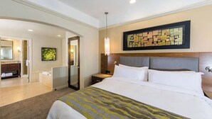 Ein Hotelzimmer mit einem großen Bett, einem Nachttisch, einem Spiegel und einem an der Wand hängenden Kunstwerk.