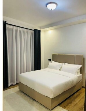 A bedroom with a bed, curtains, and a ceiling light. - Tastefully furnished 2 bedroom apartment in  Kilimani (Nairobi)