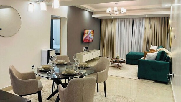 A modern living room with a green sofa, a dining area with a glass table and chairs, and a large mirror on the wall. - Tastefully furnished 2 bedroom apartment in  Kilimani (Nairobi)
