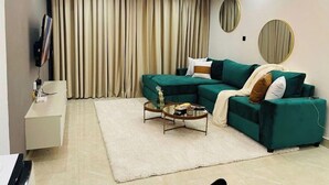 A modern living room with a sectional sofa, a round coffee table, a TV, and a large window with curtains. - Tastefully furnished 2 bedroom apartment in  Kilimani (Nairobi)
