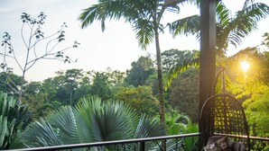 Un balcon agrémenté d’un fauteuil suspendu, entouré d’une végétation tropicale luxuriante et offrant une vue sur une zone boisée.