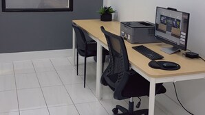 Un espacio de oficina moderno con una mesa larga, dos sillas, una computadora de escritorio e impresora.
