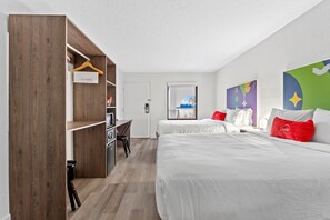 A hotel room with two beds, a wooden wardrobe, a desk, and a view of the city. - Baymont by Wyndham Jacksonville Airport (Jacksonville)