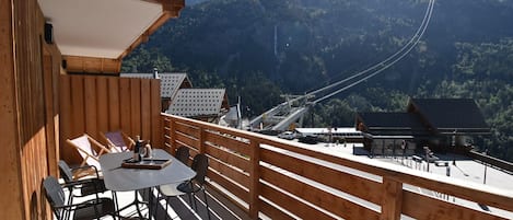 Eine Holzterrasse mit Tisch und Stühlen mit Blick auf eine Berglandschaft und eine Seilbahn.