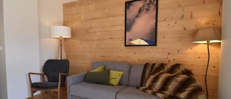 Un salon chaleureux avec un canapé gris, un mur en bois, un tableau encadré et une lampe sur pied.