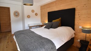A bedroom with a large bed, wooden panel walls, a white bedside table, and two bedside lamps. - L'Étendard  appartement 7 (Vaujany)