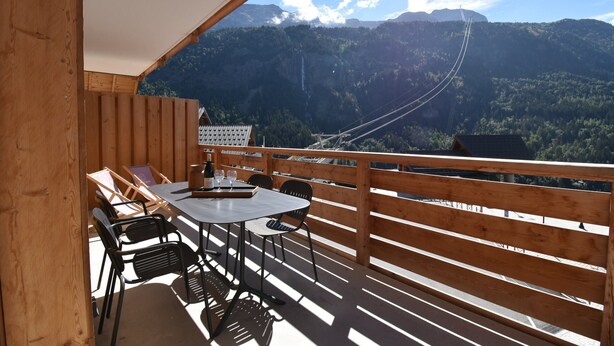 A wooden deck with a table and chairs, overlooking a mountainous landscape with a cable car in the distance. - L'Étendard  appartement 7 (Vaujany)