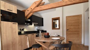 A modern kitchen with wooden cabinets, a Bosch dishwasher, and a dining area with a round table and two chairs. - L'Étendard  appartement 7 (Vaujany)