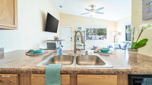 A kitchen with granite countertops, stainless steel sinks, a ceiling fan, and a flat-screen TV mounted on the wall. - 5 Min Walk to Sand | King Bed | Private Yard! (Panama City Beach)