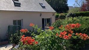 Une maison avec un toit en pente, un petit porche et un jardin orné de fleurs rouges.