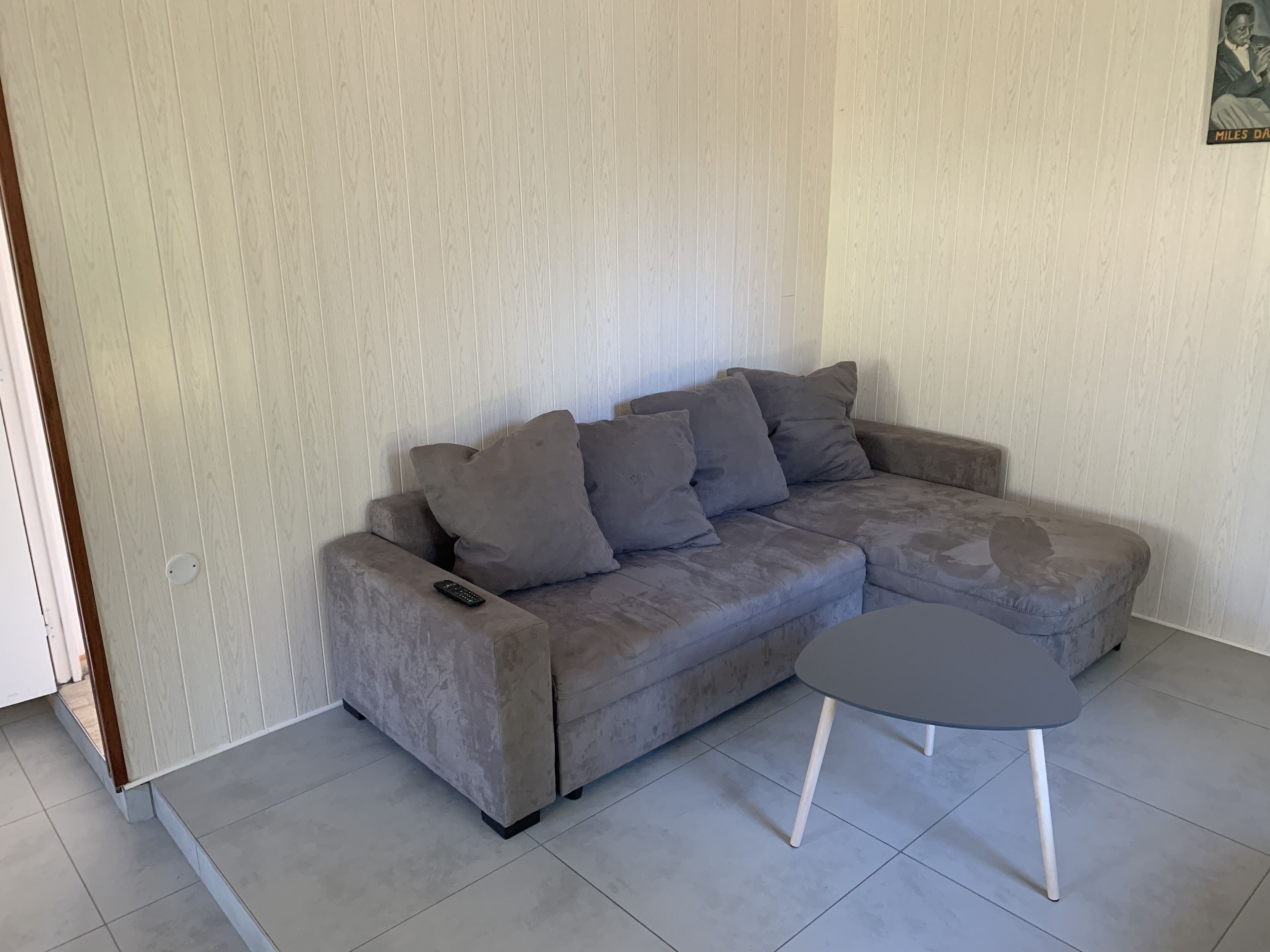 A grey sectional sofa with multiple cushions, a remote control on the armrest, and a small round table with white legs.