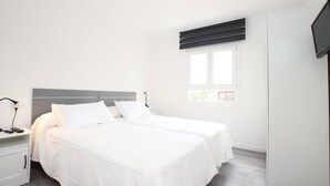 A bedroom with two beds, a nightstand, a TV, and a window with blinds. - Apartamento Rieres, Modern apartment next to the beach Port Pollensa (Port de Pollença)