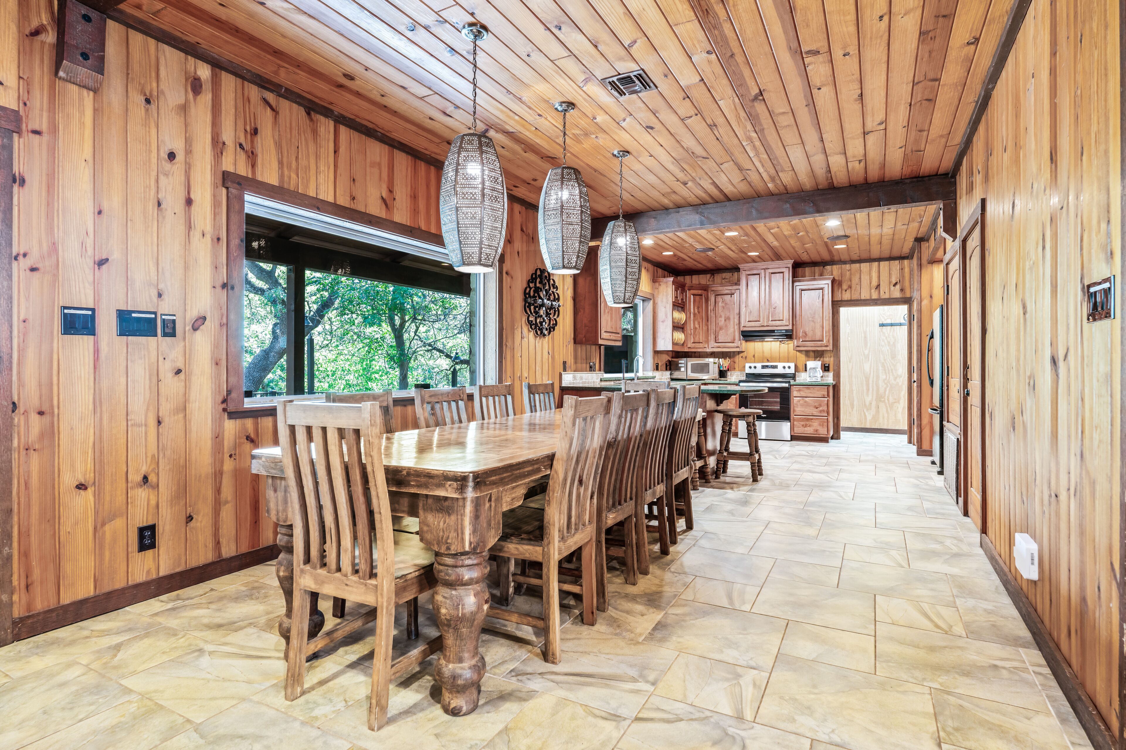 Un intérieur spacieux en bois, avec une grande table à manger et des chaises, un coin cuisine et une vue sur l’extérieur.