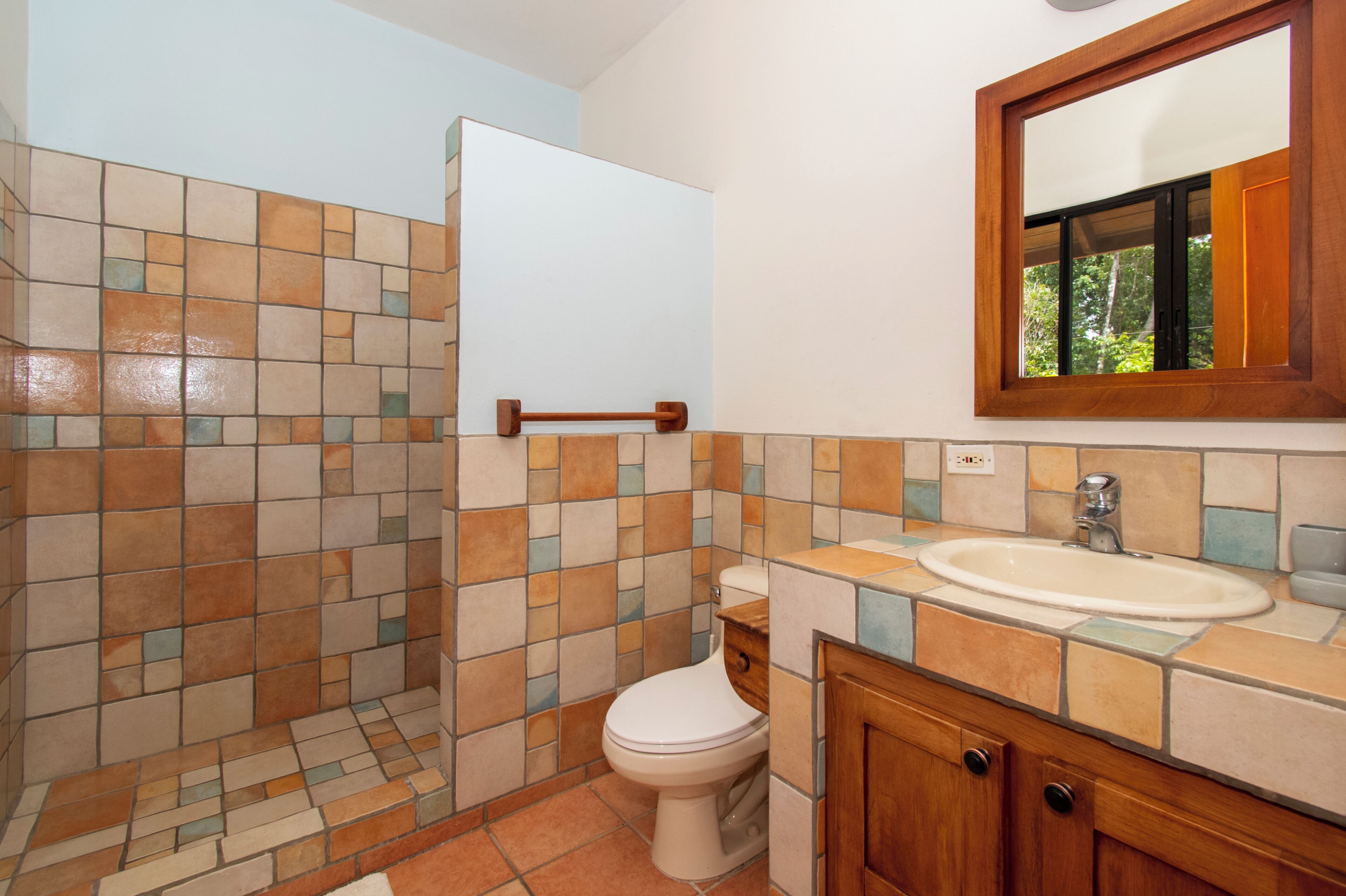 Une salle de bain avec un mur de douche carrelé, des toilettes, un lavabo et un meuble en bois.