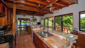 A spacious kitchen with wooden cabinets, a large island with a sink, and a ceiling fan. - 4 bdrs, Casa Shanti, ocean view & large pool! (Savegre de Aguirre)