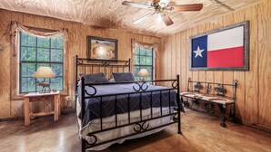 A wooden-paneled room with a bed, a ceiling fan, and a Texas flag. - Steps from THE Frio River with river access included, the perfect Concan cottage with the best price (Concan)