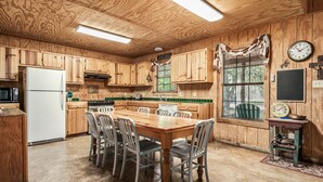 A wooden cabin-style kitchen with a central dining table, chairs, and a refrigerator. - Steps from THE Frio River with river access included, the perfect Concan cottage with the best price (Concan)