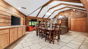 A spacious kitchen with wooden cabinets, a dining table, and chairs. There is a TV on the counter and a stone fireplace. - Directly ON THE Frio river, with a private pool and room for up to 37! (Concan)