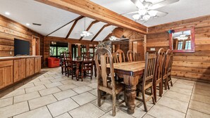A wooden interior with a dining table, chairs, a ceiling fan, and a television. - Directly ON THE Frio river, with a private pool and room for up to 37! (Concan)