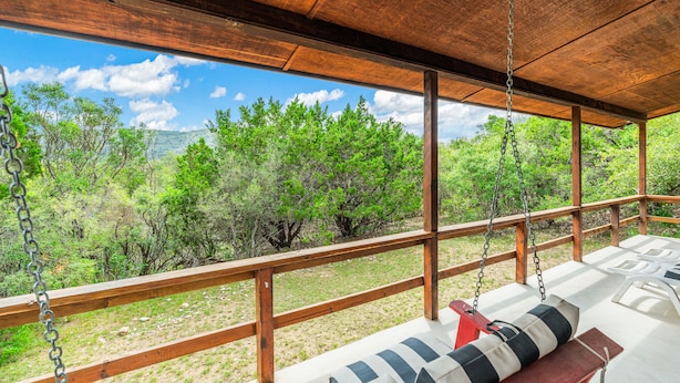 A wooden deck with a swing chair and a view of green trees and hills. - Cottage in the heart of Concan surrounded by nature & less than 5-minute drive to THE Frio River (Concan)