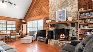 A cozy living room with a stone fireplace, wooden ceiling, and a bookshelf filled with books and decorative items. - Cottage in the heart of Concan surrounded by nature & less than 5-minute drive to THE Frio River (Concan)