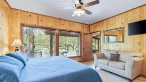 Un dormitorio con una cama, ventilador de techo, ventana, puerta y televisor en la pared.