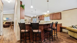 Een moderne keuken met houten kasten, een bar met barkrukken, en een eethoek met een bank en stoelen.