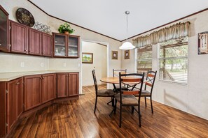 Une cuisine avec des meubles de rangement en bois, une table à manger avec des chaises et une fenêtre avec des stores.