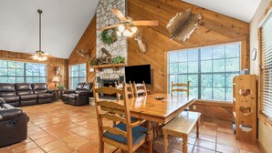 A spacious living room with a stone fireplace, wooden ceiling, and a dining area with a large table and chairs. - Directly ON the river, right in the heart of Concan, with outdoor fireplace & exclusive river access (Concan)