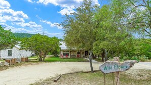 A rustic stone house with a gravel driveway and a wooden sign pointing to 'Wild Flower'. - Directly ON the river, right in the heart of Concan, with outdoor fireplace & exclusive river access (Concan)