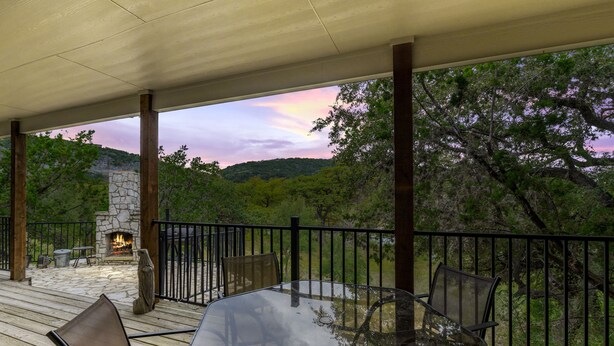A covered outdoor patio with a stone fireplace, wooden deck, and metal chairs. - Directly ON the river, right in the heart of Concan, with outdoor fireplace & exclusive river access (Concan)