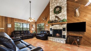 A cozy living room with leather sofas, a stone fireplace, mounted deer heads, and a television. - Directly ON the river, right in the heart of Concan, with outdoor fireplace & exclusive river access (Concan)