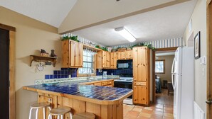 A kitchen with wooden cabinets, a tiled island with stools, a microwave, and a refrigerator. - Directly ON the river, right in the heart of Concan, with outdoor fireplace & exclusive river access (Concan)