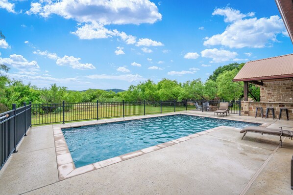 A rectangular swimming pool with a concrete deck, surrounded by a black metal fence. - Private swimming pool, huge outdoor entertainment area, less than 5-minute drive to THE Frio River (Concan)